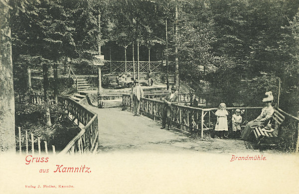 Tato pohlednice zachycuje jedno z kdysi upravených odpočinkových míst v lesoparku pod Jehlou, nazývané 'Brandmühle'. Z tehdejší úpravy dnes již nic nezůstalo.