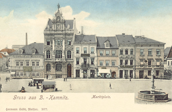 Na pohlednici České Kamenice z roku 1910 je západní strana náměstí se secesní budovou spořitelny a dnes již neexistujícím hostincem U slunce (vlevo). Stejné místo v roce 1899 si můžete prohlédnout na předchozí pohlednici.