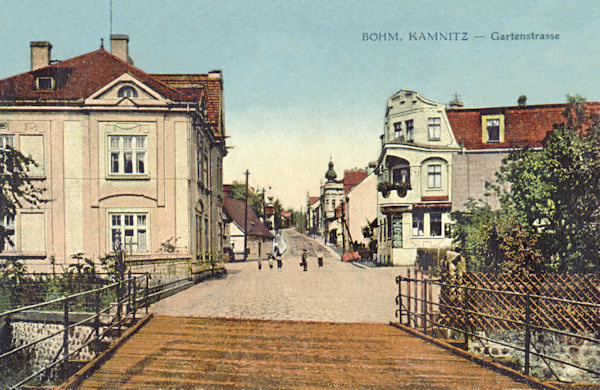 Na pohlednici České Kamenice z první čtvrtiny 20. století vidíme tehdejší Zahradní ulici (nynější ul. 5. května) s původním dřevěným mostem přes říčku Kamenici v popředí.