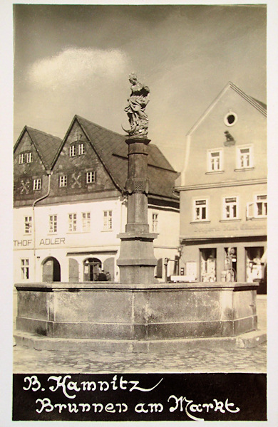 Tato pohlednice zachycuje kašnu se sochou Panny Marie uprostřed náměstí. Budova hotelu Adler v pozadí později zchátrala, v roce 1968 byla zbořena a nově postavena.