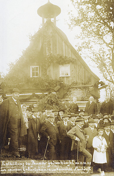 Tato pohlednice zachycuje slavnostní odhalení pamětní desky Amanda A. Paudlera na jeho rodném domku ve Vísce pod Lesy, které se uskutečnilo 13. října 1907.