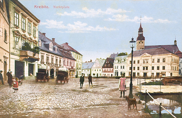 Tato pohlednice zachycuje severozápadní část náměstí v roce 1913. Většina domů zde stojí i dnes, jenom dva staré domy s vysokými štíty (uprostřed) tu již nenajdeme.