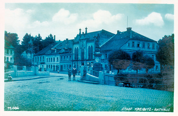 Tato pohlednice zachycuje domy na východní straně náměstí, mezi nimiž vyniká pseudogotická budova bývalé radnice z roku 1872. Vpravo od ní je rodný dům Tadeáše Haenkeho, v němž je dnes zřízeno muzeum.