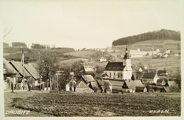 This picture postcard shows the centre of the village with the church Assumption of the Virgin Mary and the peak of the Spravedlnost-hill as seen from the Northwest. The factory building in the background had been demolished after 2000.