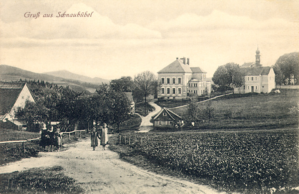 This picture postcard shows the centre of the village Sněžná as seen from the North. In the centre there ist the pretty schoolhouse and the presbytery behind of which the roof of the pilgrimage church of Our Lady of the Snows with its small tower.