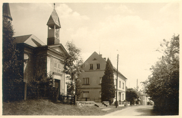 Auf dieser Ansichtskarte aus den 50er Jahren des 20. Jahrhundert sieht man die Hauptstrasse mit dem Giebel der Jungfrau Maria von Karmel- Kapelle aus dem Jahr 1870. Das Türmchen mit der Turmuhr über dem Eingang wurde 1935 angebaut.