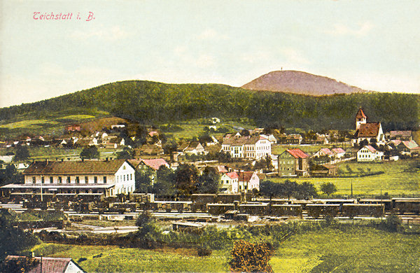 Auf dieser Ansichtskarte aus dem Jahr 1915 sieht man Rybniště (Teichstatt) mit dem Jedlová-Berg (Tannenberg) im Hintergrund. Ausser dem Bahnhof  springt aus den örtlichen Häusern noch die Schule und die St. Josephs-Kirche in die Augen.