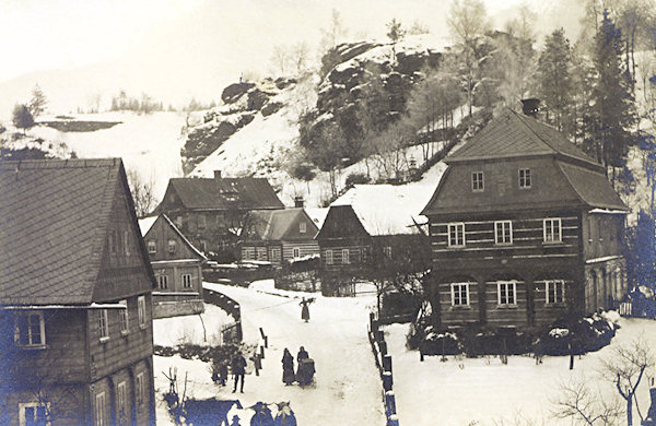 Tato zimní pohlednice zachycuje malebné zákoutí s roubenými domy u silnice do Práchně. Většina z nich dnes už bohužel neexistuje, dochovaly se pouze dva malé domky v pozadí.