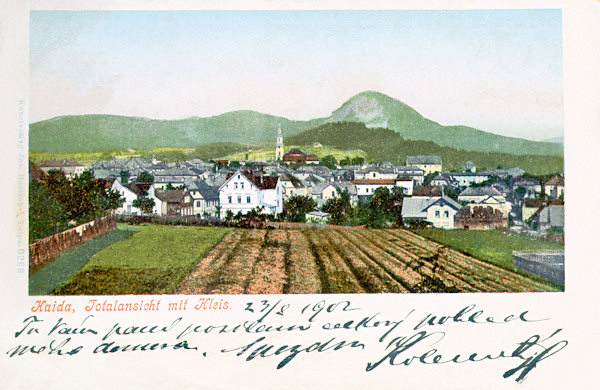 This picture postcard from the turn of the 19th and 20th century shows Nový Bor from the southern side. Over the houses rises the tower of the church Assumption of the Virgin and to the right behind it the low Borský vrch-hill, on the horizon rises the prominent cone of the Klíč-hill.