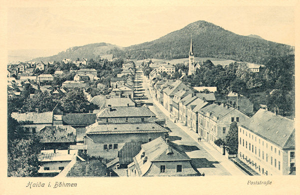 This picture postcard from the 20s of the 20th century shows the then Post street leading from the town square in the direction to Česká Lípa as seen from the tower of the church of the Assumption of the Virgin. In the background the tower of the Protestant church is seen which later, in 1982, had been destroyed by fire, and on the horizon there rises the Chotovický vrch-hill.