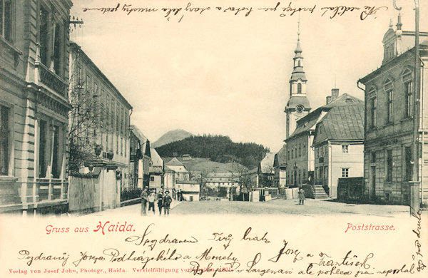 This picture postcard from 1901 shows the beginning of the street then named Poststrasse (at present T.G. Masaryk-street) not long before the start of the construction of the new savings bank building. To the right the tower of the church Asumption of the Virgin in looking over the houses.