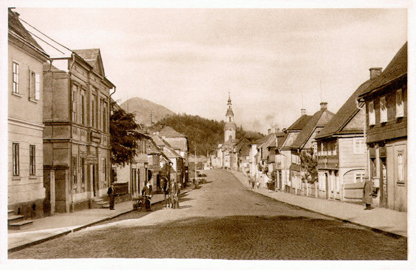 This picture postcard shows the original houses of the former Poststrasse (at present T. G. Masaryk-street) leading from the market place in the direction to Česká Lípa. The houses on the right side were in the 70ies of the 20th century demolished to make place for a group of prefabricated buildings. In the background the church Asumption of the Virgin at the market place is seen.