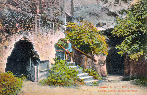 Tato pohlednice zachycuje v současné době nepřístupný skalní dvůr na severní straně Poustevnického kamene. Mezi vchody do vytesaných místností vedou schody k úzké spáře s Rytířským schodištěm, vystupujícím na vrchol skály.