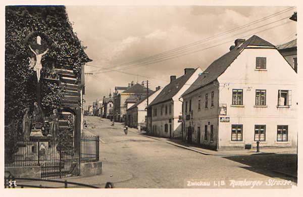 This picture postcard shows the central part of the present-day Komenský-street which, however at present looks differently. The timbered house with the decorated Cross disappeared and also the two next houses on the right side of the street had been demolished.