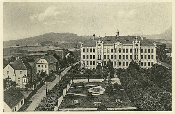This picture postcard shows the primary and lower secondary school of Cvikov with the adjacent park as seen from the tower of the church St. Elizabeth. On the left side we see the houses of the Čechova ulice street which at present immediately at the school is crossed by the newly built bypass road.