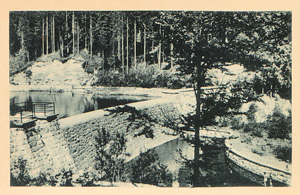 Tato pohlednice zachycuje zděnou hráz vodní nádrže, vybudovanou v úzkém údolí Hamerského potoka v letech 1937-38. Přehrada sloužila k pohonu mlýna a pily v níže ležícím Hamru.