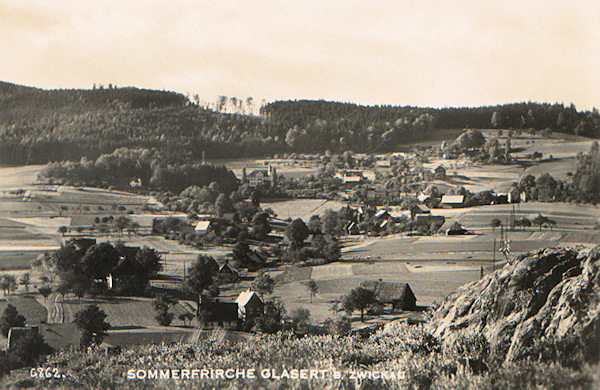 This picture postcard shows the view of the village Trávník from the southeast. Almost in the centre of the picture we see the manor-house called „Zámeček“. In the background behind of it there is a wooded projection of the Trávnický vrch hill.