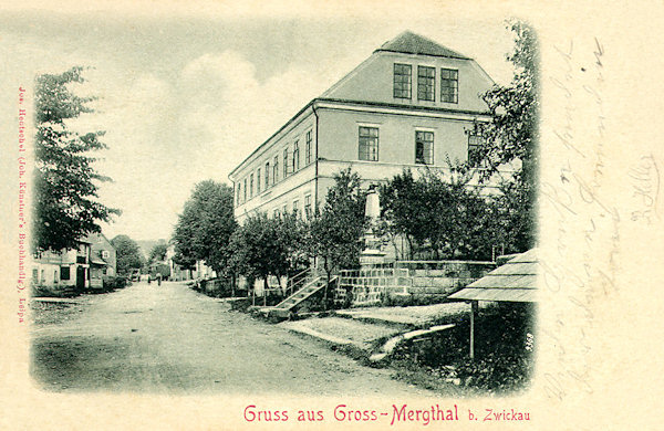 Pohlednice z roku 1901 zachycuje hlavní ulici uprostřed obce s výstavnou budovou školy a bývalým válečným pomníkem.