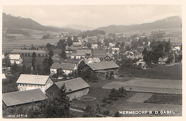 Na této pohlednici vidíme Heřmanice ze zalesněného návrší Březina (Heidebüschel) nad východním okrajem osady. V pozadí vpravo vyčnívá Zámecký vrch.