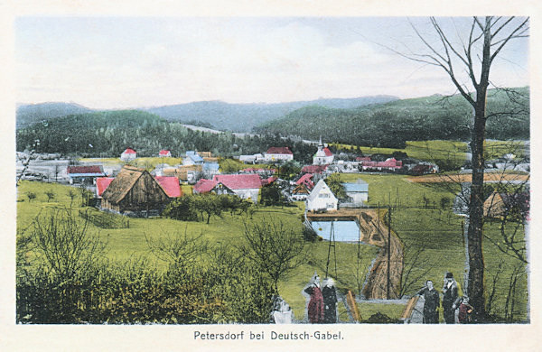 Tato pohlednice z doby před rokem 1930 zachycuje Petrovice s kostelem Nejsvětější Trojice od západu z úpatí vrchu Sokol.