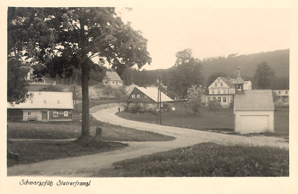 Auf dieser Ansichtskarte sieht man die Ortsmitte mit der Kapelle und dem Hotel 'Steyrer Franzl' kurz nach der Fertigstellung der Strasse von Rynoltice (Ringelshain) nach Hrádek nad Nisou (Grottau).