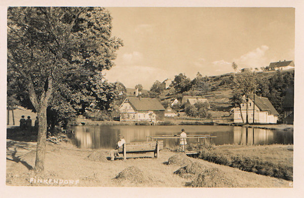 This picture postcard shows the pond in the centre of the village which also to-day serves for occasional bathing. The house on the right behind of the pool at present does not more exist and the slope in the background is overgrown with wood.