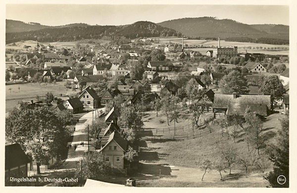 Diese Ansichtskarte von 1932 zeigt die Gemeinde von Süden gesehen. Im Vordergrund sieht man die Strasse nach Janovice, im Hintergrund ragt das Gebäude der Schicht'schen Seifenfabrik empor und der Horizont hinter ihr wird vom Kamm des Lausitzer Gebirges mit dem Pískové návrší abgeschlossen.