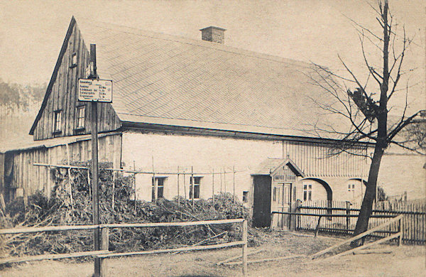 This picture postcard shows a typical house of the village Horní Sedlo. In the left part the picture shows how people of Horní Sedlo with means of a covering of branches protected the walls of their houses against freezing through during the long winter. In the foreground there is a direction indicator of the mountain ridge wandering path passing along here.