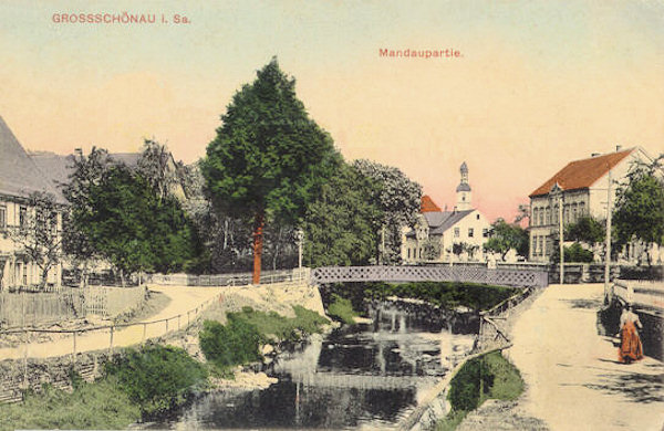 Na pohlednici z roku 1911 jsou domy kolem toku Mandavy s mostem. V pozadí vyčnívá věž kostela.