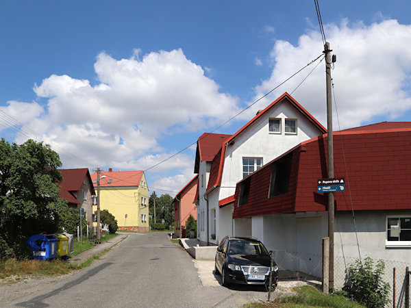Häuser an der Straße im oberen Teil des Dorfes. Auf der rechten Seite befand sich früher ein Geschäft, und im Hintergrund ist das gelbe Gebäude der ehemaligen Schule zu sehen.